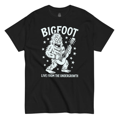 Bigfoot Live From The Undergrowth T-shirt featuring cartoon Sasquatch playing guitar surrounded by stars, white print on black background.